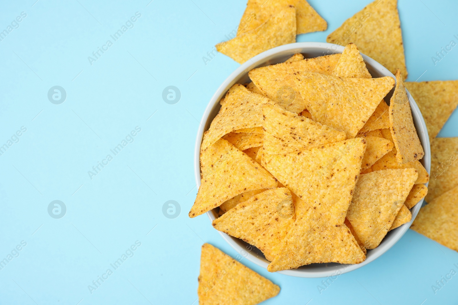Photo of Bowl with tasty Mexican nachos chips on light blue background, flat lay. Space for text