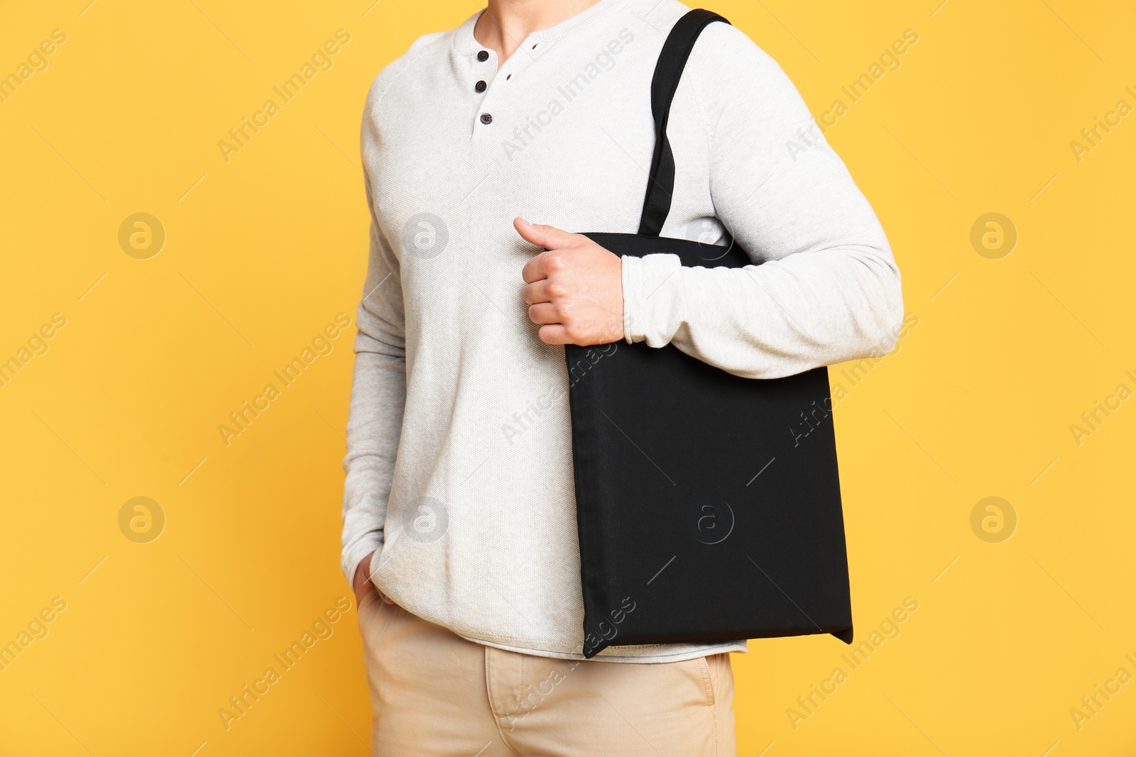 Photo of Young man with eco bag on yellow background, closeup