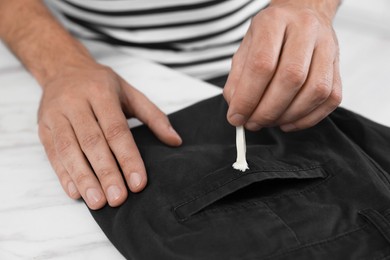 Man removing chewing gum from black jeans at white marble table, closeup