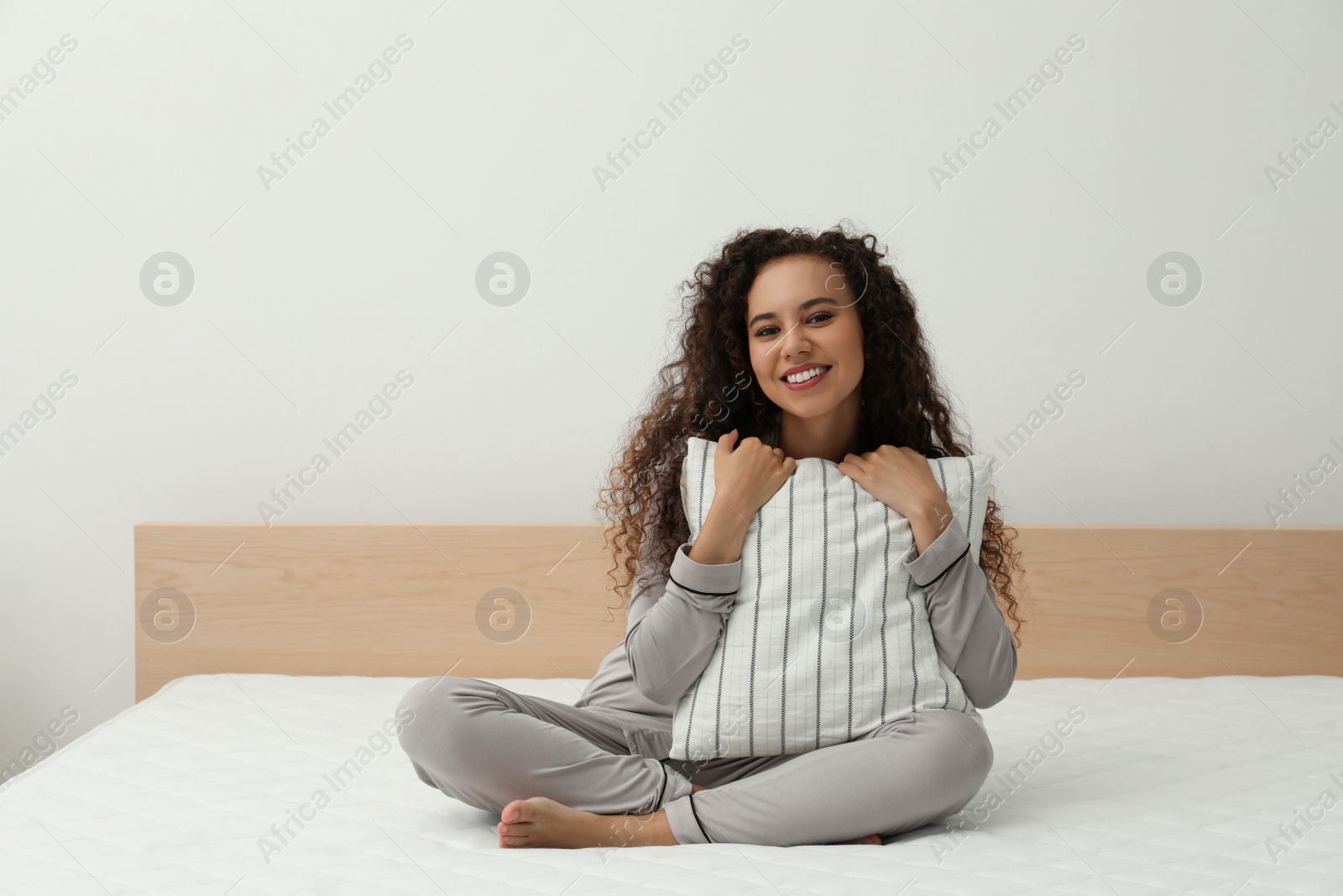 Photo of Happy young African American woman hugging pillow on bed with comfortable mattress at home