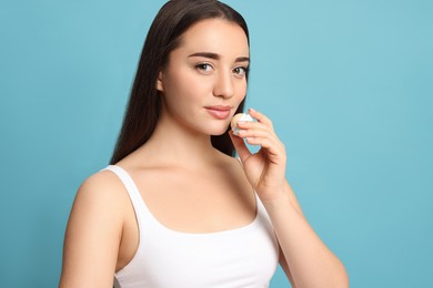 Photo of Young woman applying lip balm on turquoise background