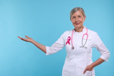 Doctor with pink ribbon and stethoscope on light blue background. Breast cancer awareness
