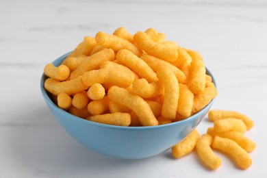 Photo of Many tasty cheesy corn puffs on white marble table