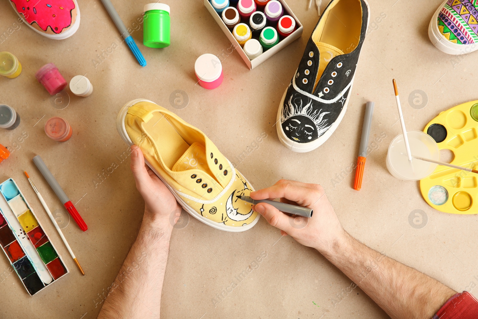 Photo of Man painting on sneaker at table, top view. Customized shoes