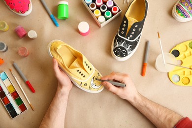 Photo of Man painting on sneaker at table, top view. Customized shoes