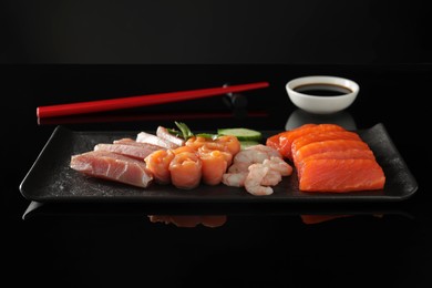 Photo of Delicious sashimi set of salmon, tuna and shrimps served with cucumbers, parsley and soy sauce on black mirror surface