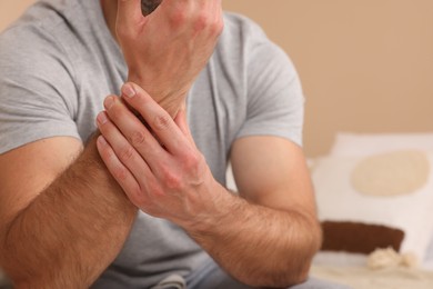 Photo of Man suffering from pain in his hand on bed indoors, closeup