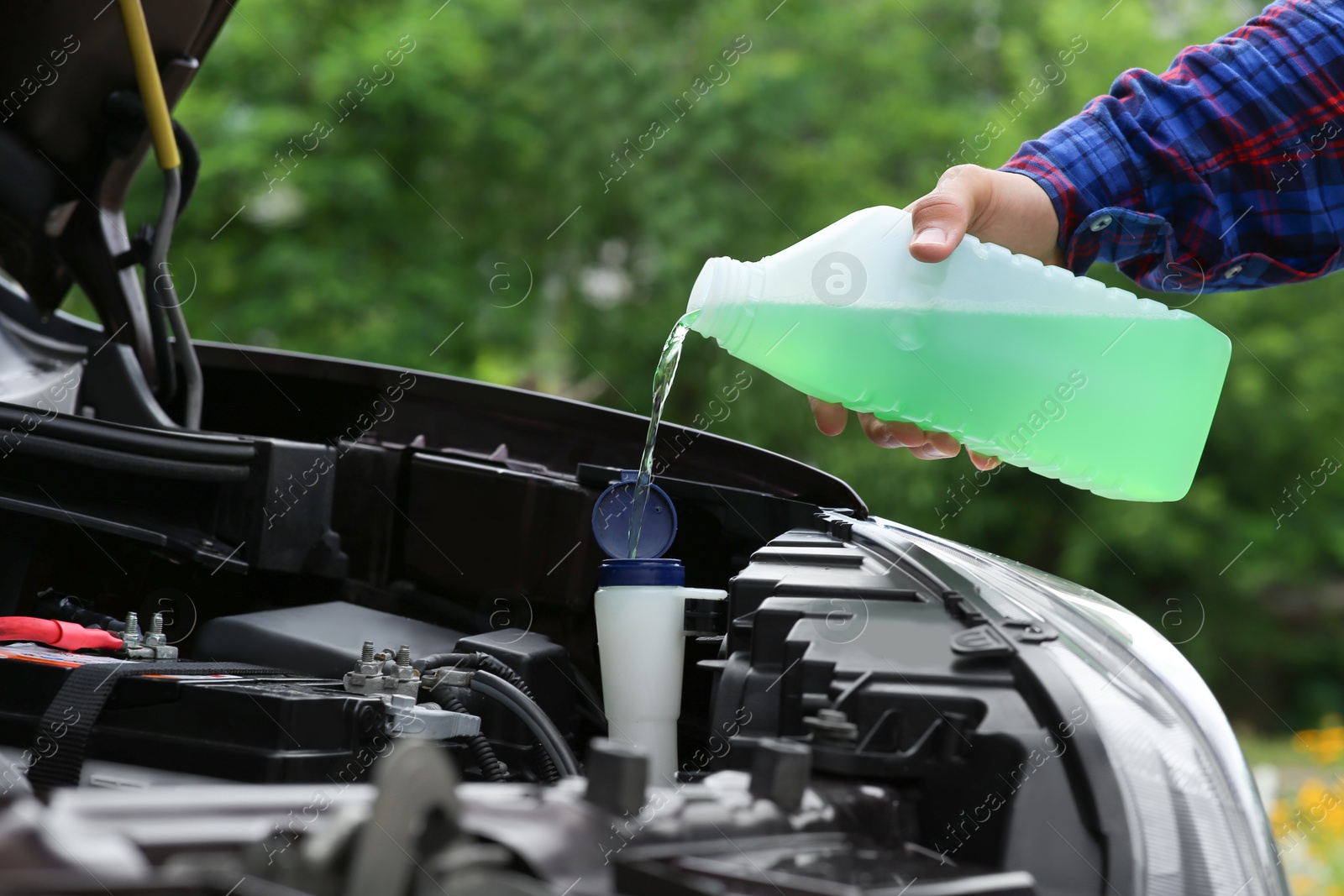 Photo of Man pouring liquid from plastic canister into car washer fluid reservoir, closeup