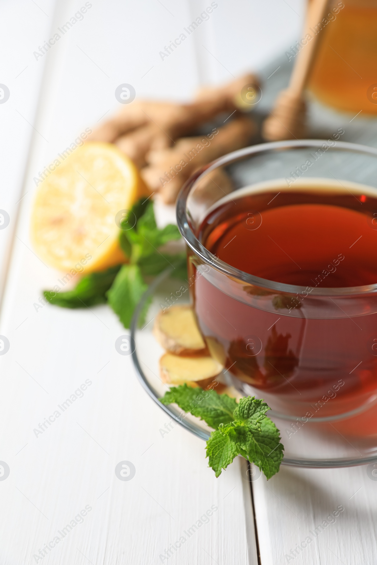 Photo of Cup of delicious ginger tea and ingredients on white wooden table, closeup