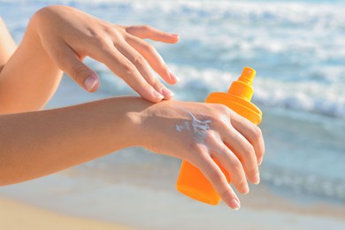 Photo of Woman applying sun protection cream on her hand at beach, closeup