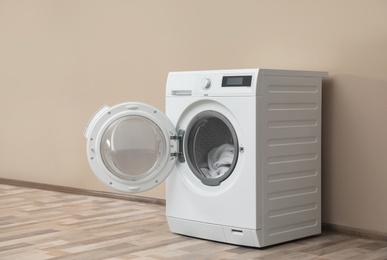 Photo of Modern washing machine with laundry near color wall, space for text