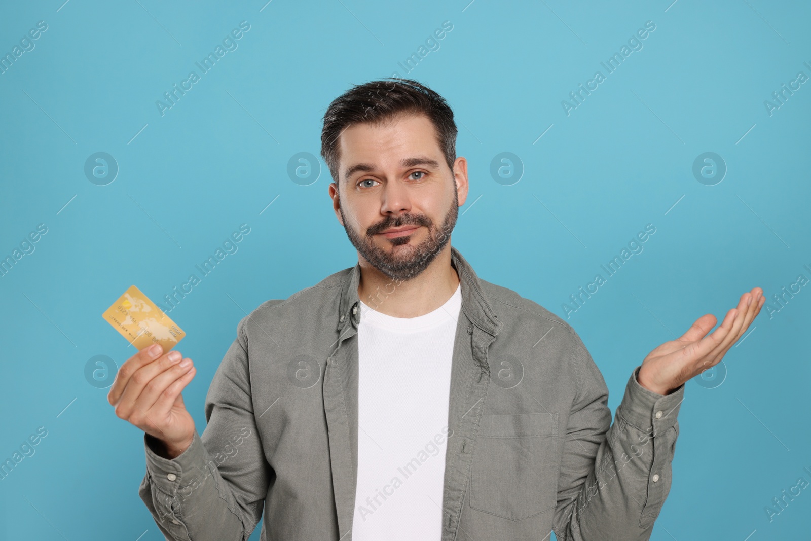 Photo of Confused man with credit card on light blue background. Debt problem