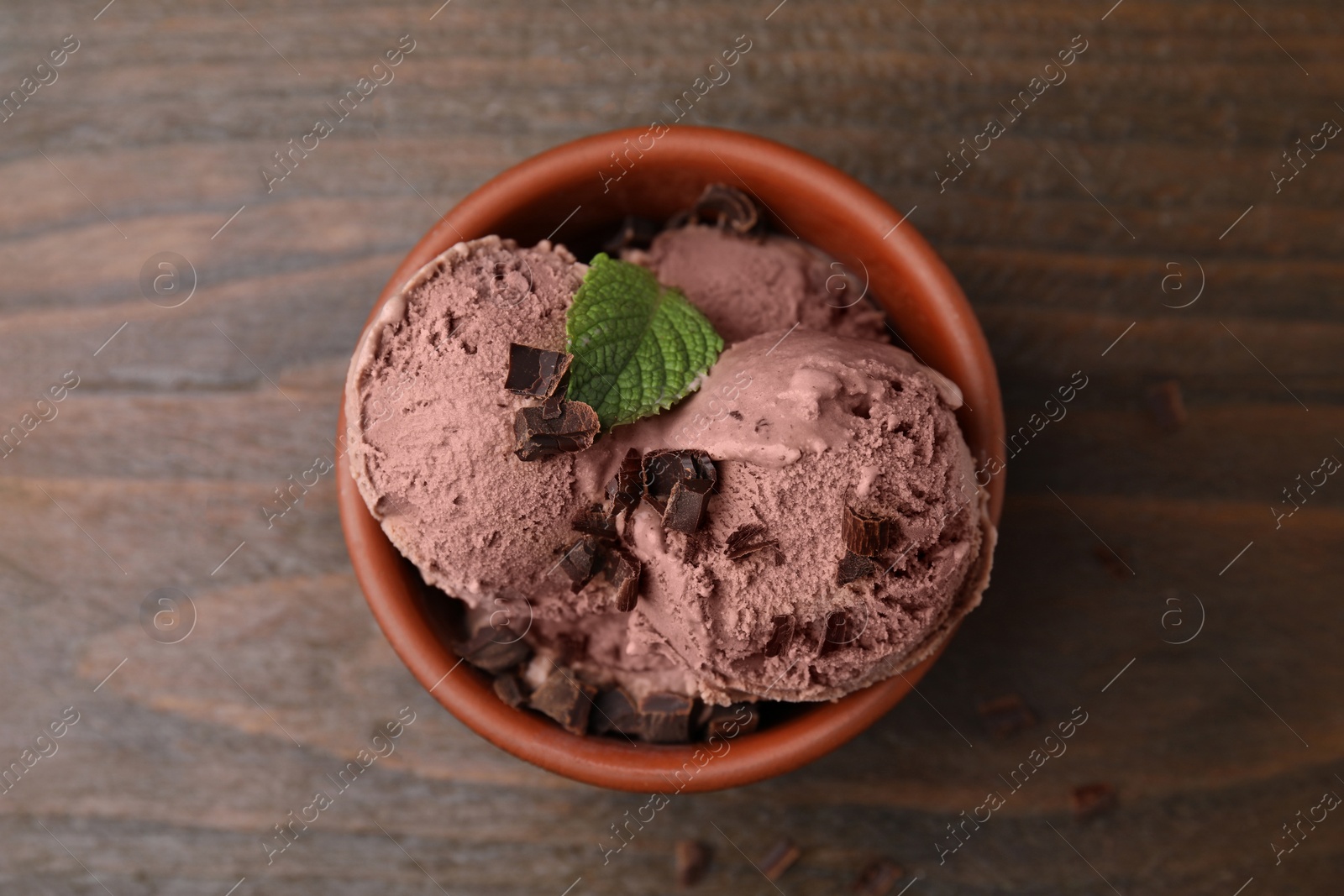 Photo of Bowl of tasty ice cream with chocolate chunks and mint on wooden table, top view