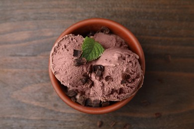 Photo of Bowl of tasty ice cream with chocolate chunks and mint on wooden table, top view