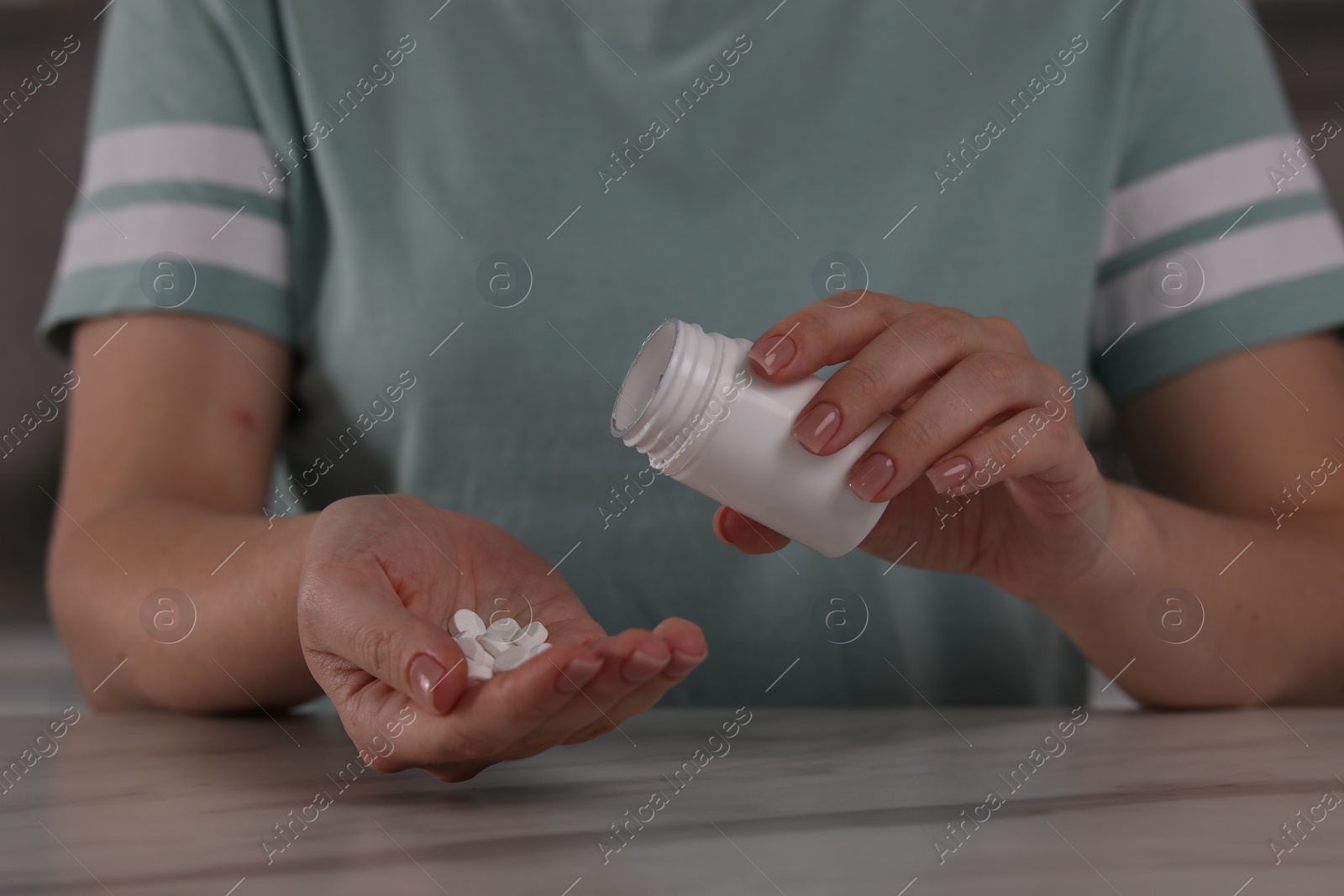 Photo of Woman pouring antidepressants from bottle at table, closeup