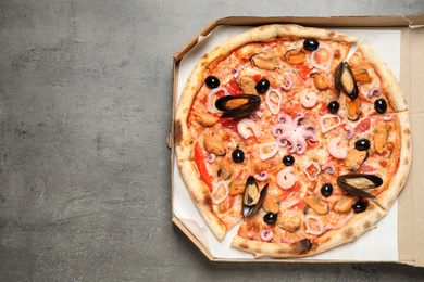 Photo of Delicious seafood pizza in box on grey table, top view. Space for text