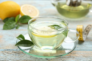 Photo of Glass cup of diet herbal tea with green leaves and lemon on wooden table