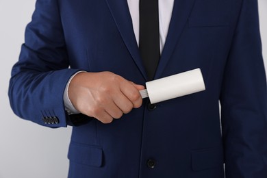 Man cleaning suit with lint roller on light grey background, closeup