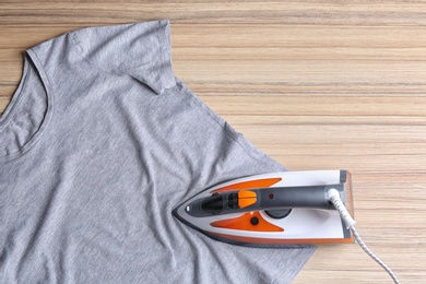 Photo of Flat lay composition with modern electric iron and t-shirt on wooden table. Space for text