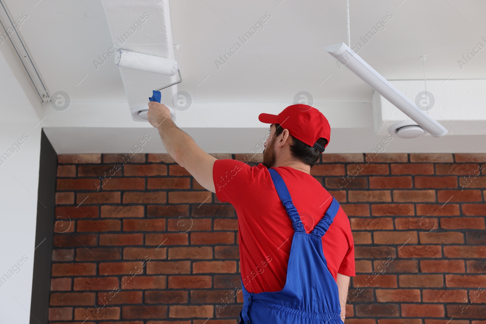 Photo of Handyman painting ceiling with roller in room, back view