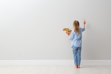 Photo of Little girl painting on light grey wall indoors, back view. Space for text