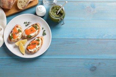 Photo of Delicious bruschettas with cream cheese, salmon and pesto sauce on light blue wooden table, flat lay. Space for text