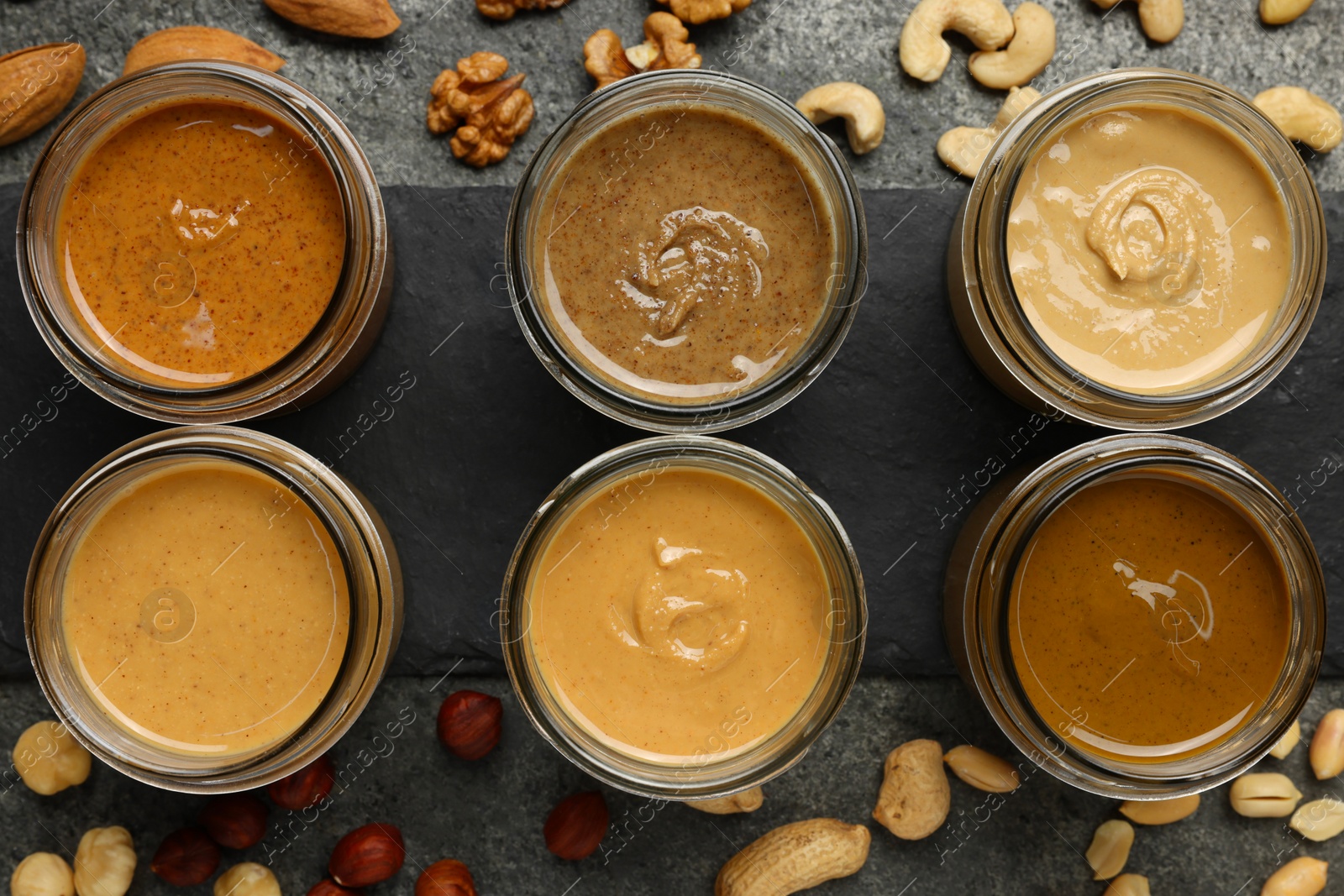 Photo of Tasty nut butters in jars and raw nuts on gray table, flat lay