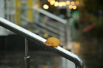 Photo of Wet metal handrail with fallen leaf after rain outdoors, closeup