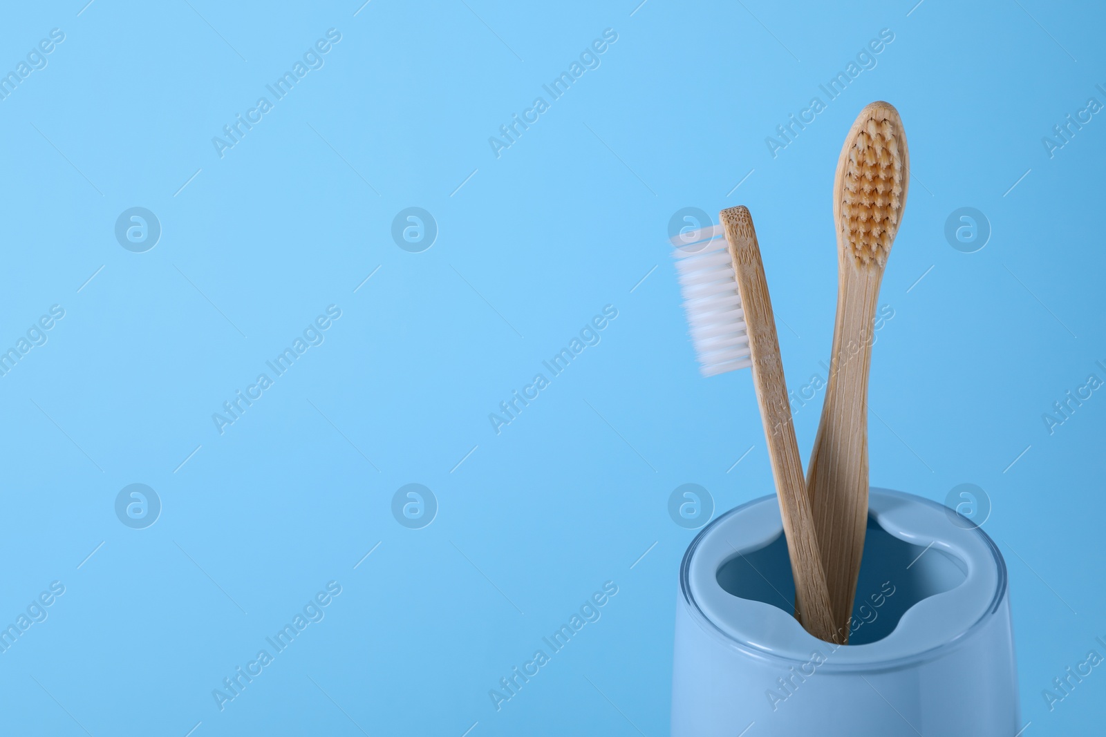 Photo of Bamboo toothbrushes in holder on light blue background, space for text