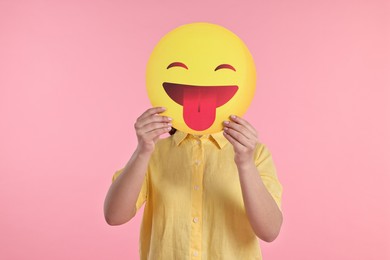 Photo of Woman covering face with emoticon sticking out tongue on pink background