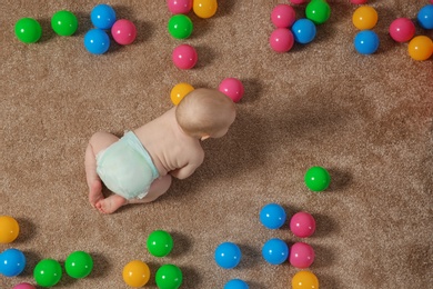 Photo of Cute little baby crawling on carpet with toys, top view