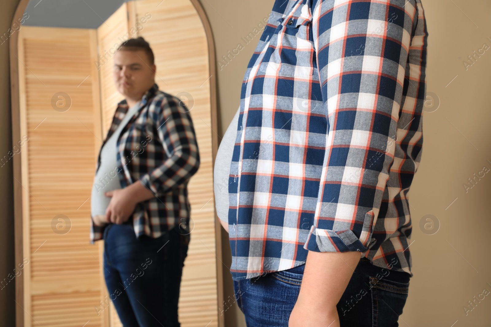 Photo of Overweight man in tight t-shirt near mirror at home