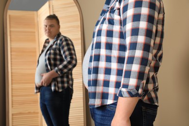 Photo of Overweight man in tight t-shirt near mirror at home