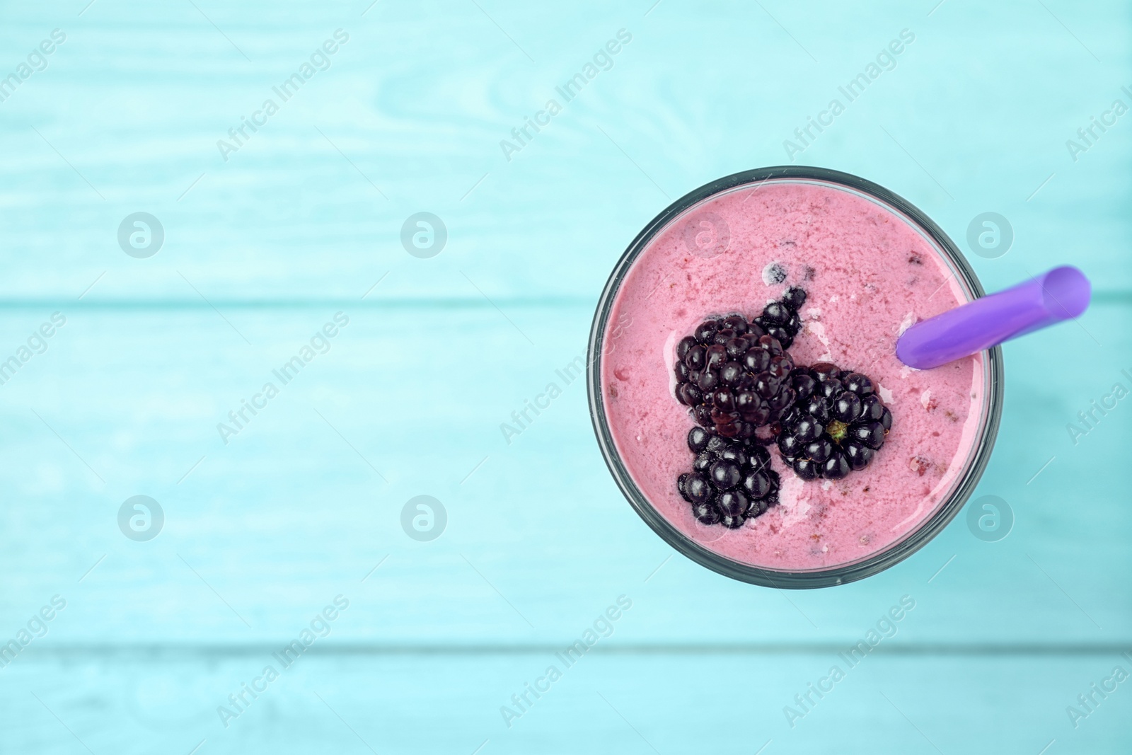 Photo of Glass of delicious blackberry smoothie on light blue wooden background, top view. Space for text