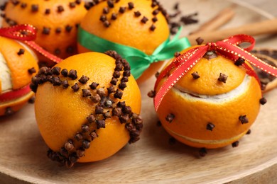 Pomander balls made of tangerines with cloves on wooden plate, closeup