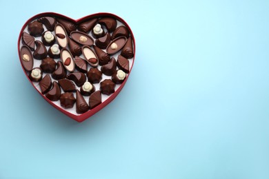 Heart shaped box with delicious chocolate candies on light blue background, top view. Space for text