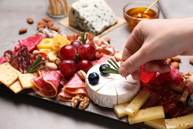 Photo of Woman putting rosemary on board with different appetizers, closeup