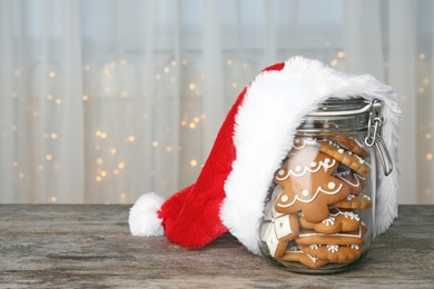 Photo of Glass jar with tasty homemade Christmas cookies and Santa hat on table