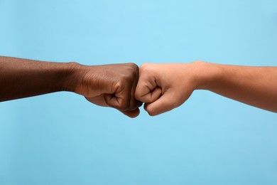 Photo of Men making fist bump on light blue background, closeup