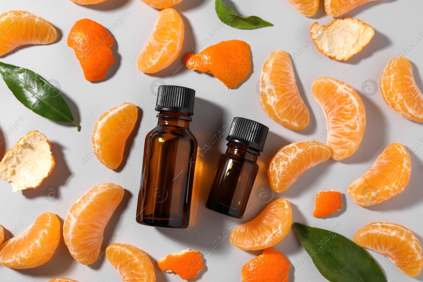 Photo of Aromatic tangerine essential oil in bottles, leaves and citrus fruit on grey table, flat lay