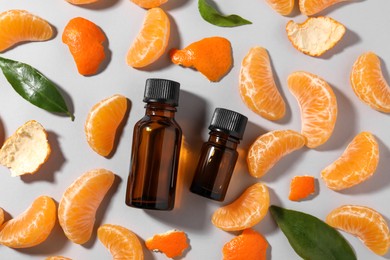 Photo of Aromatic tangerine essential oil in bottles, leaves and citrus fruit on grey table, flat lay