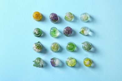 Photo of Ice cubes with flowers and leaves on light blue background, flat lay