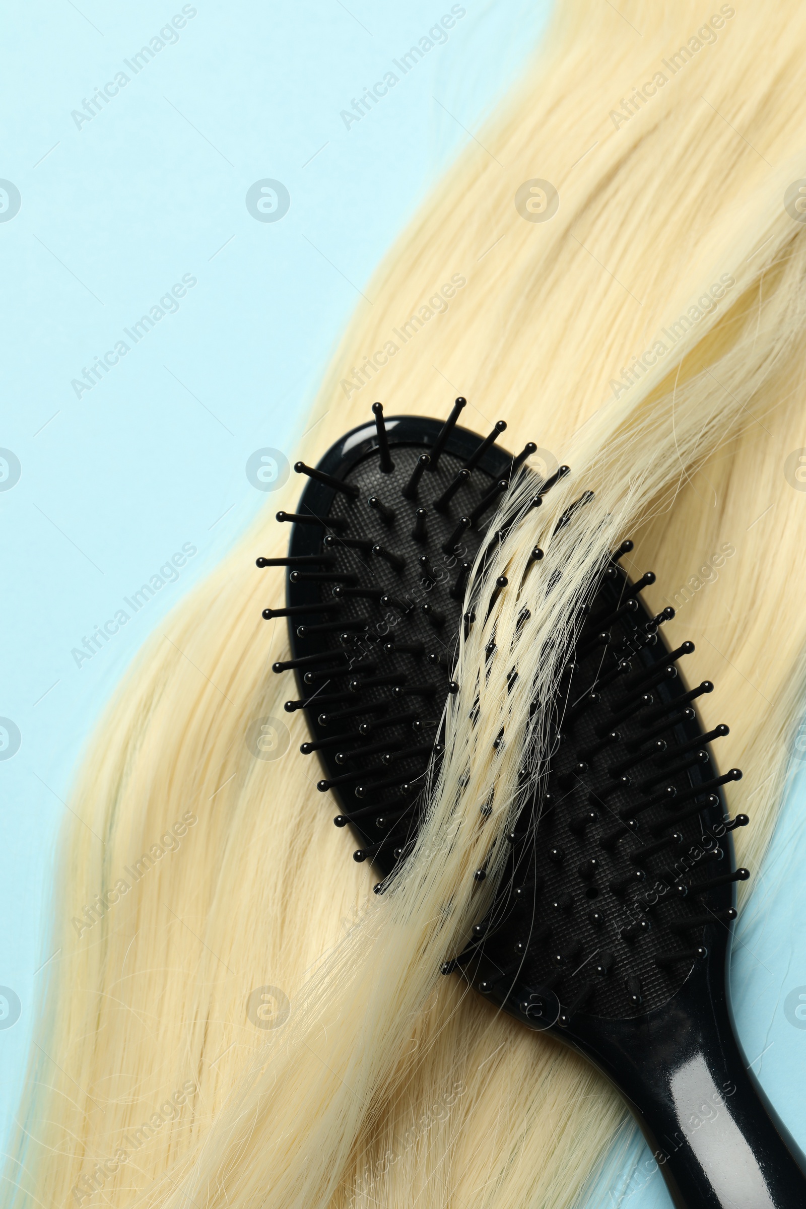 Photo of Stylish brush with blonde hair strand on light blue background, top view