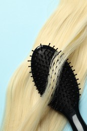 Stylish brush with blonde hair strand on light blue background, top view