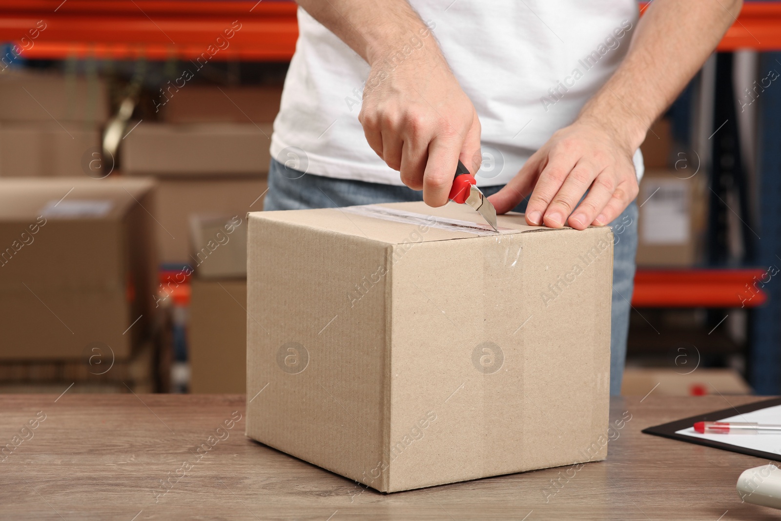 Photo of Post office worker with utility knife opening parcel at counter indoors, closeup