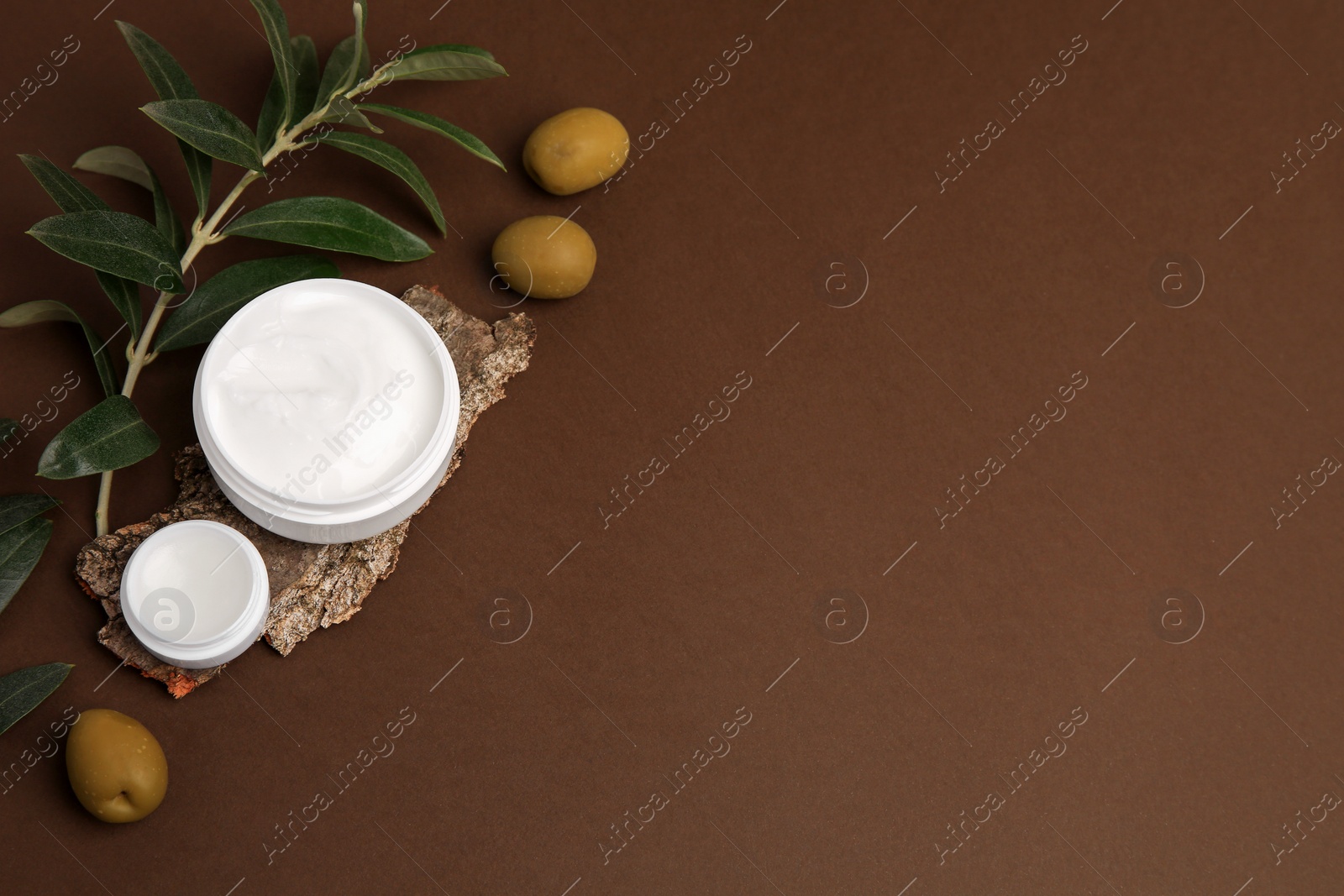 Photo of Flat lay composition with jars of cream and olives on brown background. Space for text