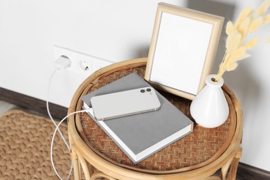 Photo of Modern smartphone charging on round rattan table indoors