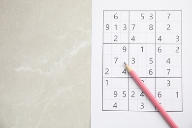 Photo of Sudoku and pencil on light marble table, top view. Space for text