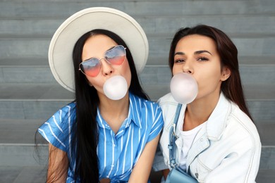 Photo of Stylish women blowing gums near stairs outdoors