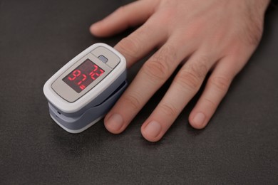 Man measuring oxygen level with modern fingertip pulse oximeter at grey table, closeup